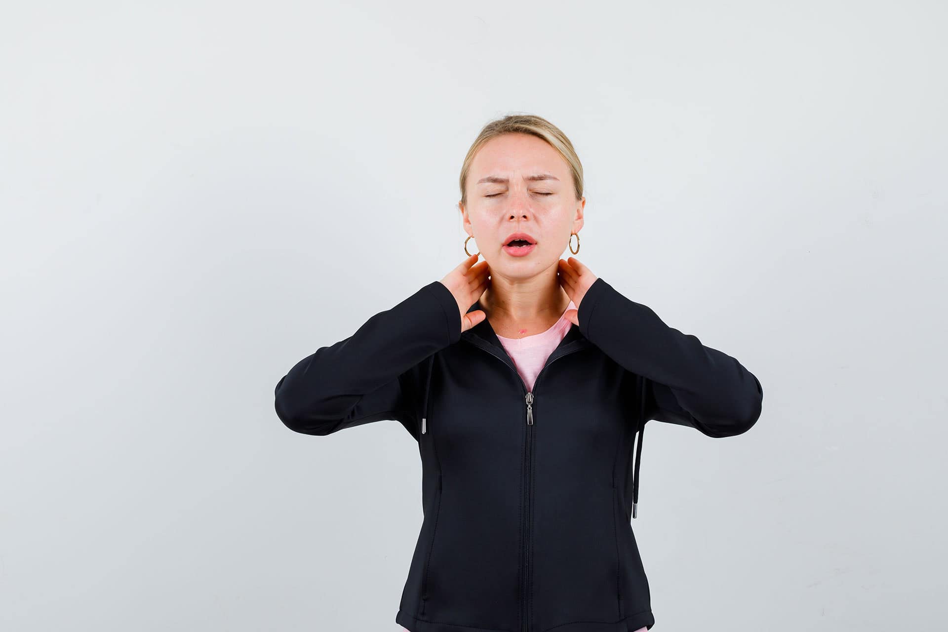 Young woman holding her neck with her hands, experiencing neck discomfort, in a clinic setting.